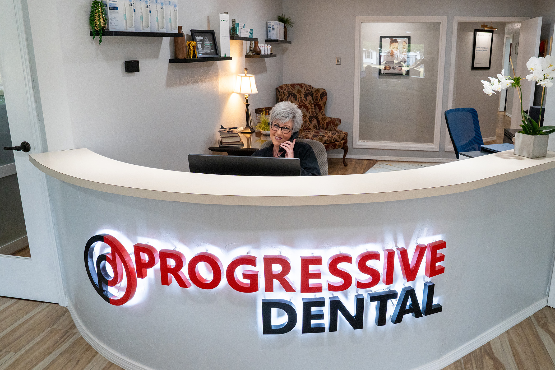 Receptionist on the phone behind a curved front desk with a “Progressive Dental” sign, welcoming dentist without insurance Oklahoma City patients in a modern dental office lobby.