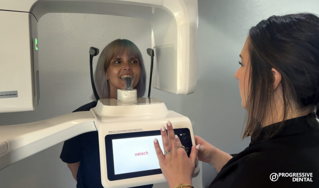 A dental assistant operates a panoramic X-ray machine for a patient interested in affordable dental implants as they bite into the mouth guard.