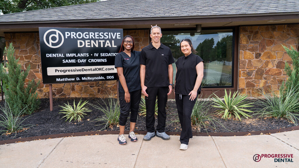 Three staff members in black uniforms stand in front of a Progressive Dental sign at an Oklahoma City cosmetic dentist office.