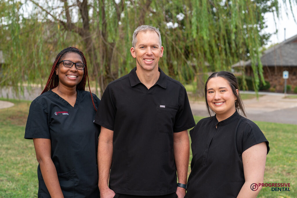 Three staff members of Progressive Dental stand outdoors in black medical scrubs, representing Oklahoma City cosmetic dentistry options.