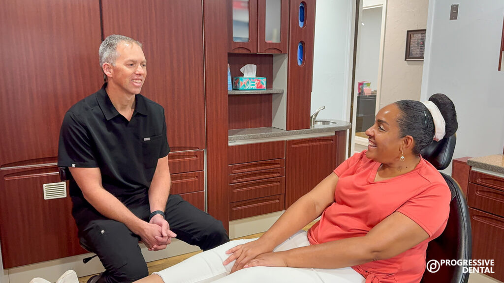 A dentist in black scrubs talks with a patient in an orange shirt during their first dental visit Oklahoma City, seated in a modern office.