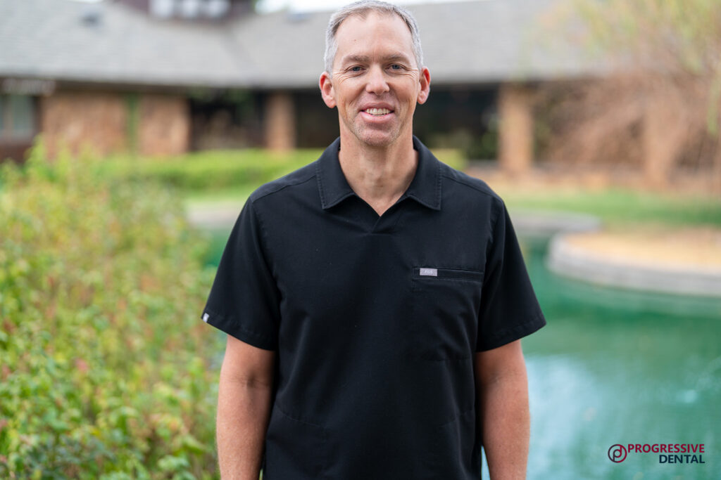 An Oklahoma City cosmetic dentist smiles while wearing a black scrub top outdoors near a pond.
